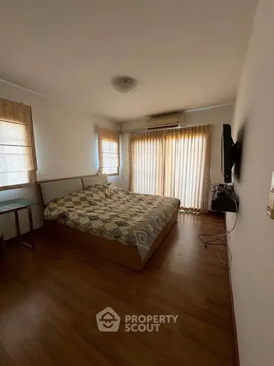 Spacious bedroom with large windows and wooden flooring, featuring a cozy bed and modern TV setup.