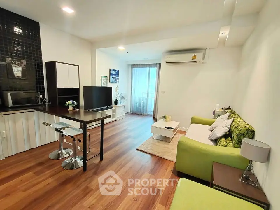 Modern living room with green sofa, wooden flooring, and open kitchen layout in a cozy apartment.