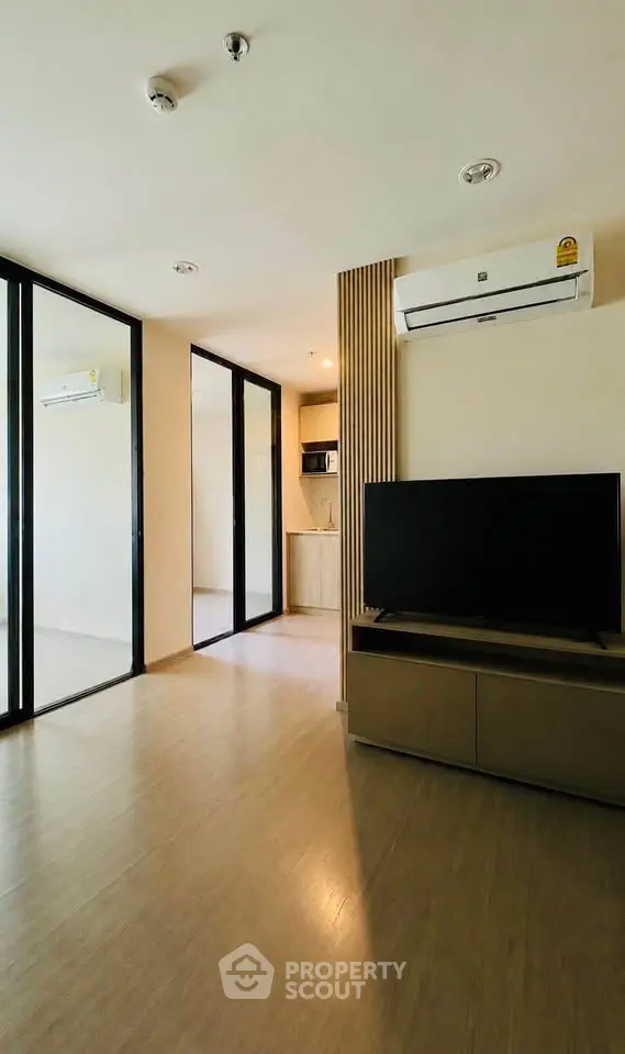 Modern living room with sleek design and air conditioning, featuring a TV and open layout leading to a kitchen.