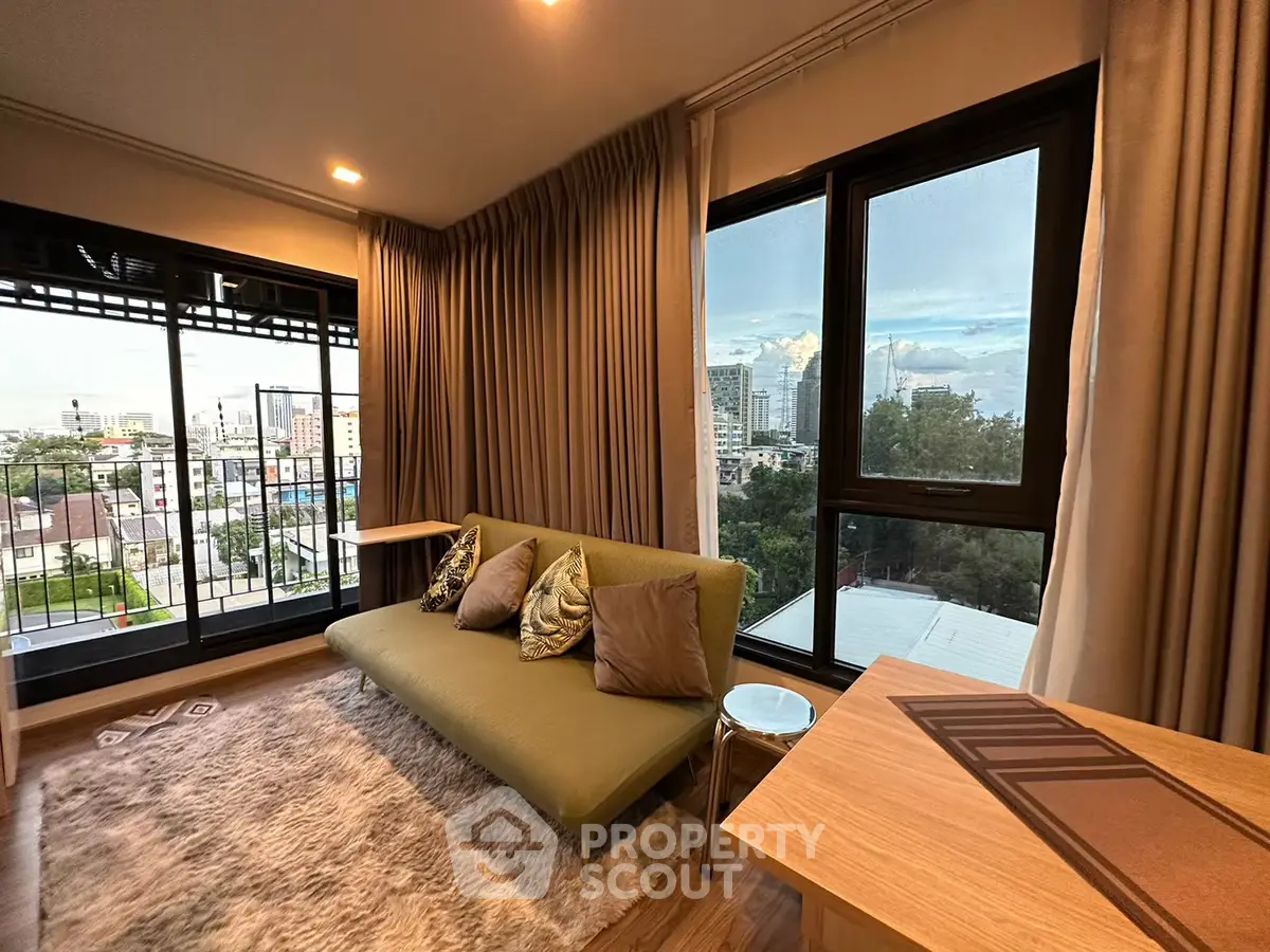 Modern living room with large windows and city view, featuring a cozy sofa and stylish decor.