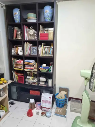 Cozy storage area with bookshelf and fan in a well-organized room.