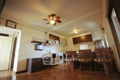 Spacious open-layout living room with modern kitchen and dining area, featuring wooden flooring and ceiling fan.