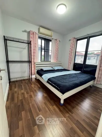 Cozy bedroom with wooden flooring and large windows for natural light.