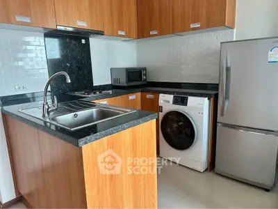 Modern kitchen with wooden cabinets, granite countertops, and built-in appliances including washing machine and fridge.