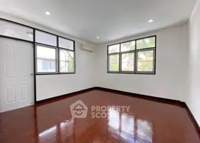 Spacious empty room with polished wooden floors and large windows offering natural light.
