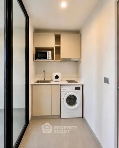 Modern compact kitchen with washing machine and microwave in sleek apartment.