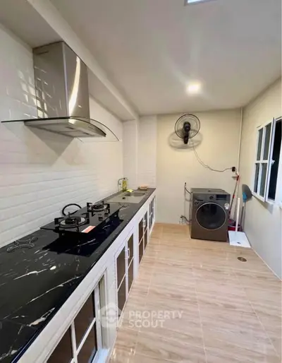 Modern kitchen with gas stove and washing machine, sleek countertops, and ample storage space.