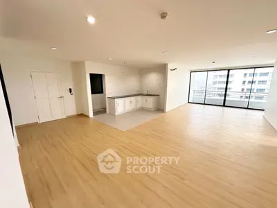 Spacious open-plan living area with wooden flooring and large windows offering city views.