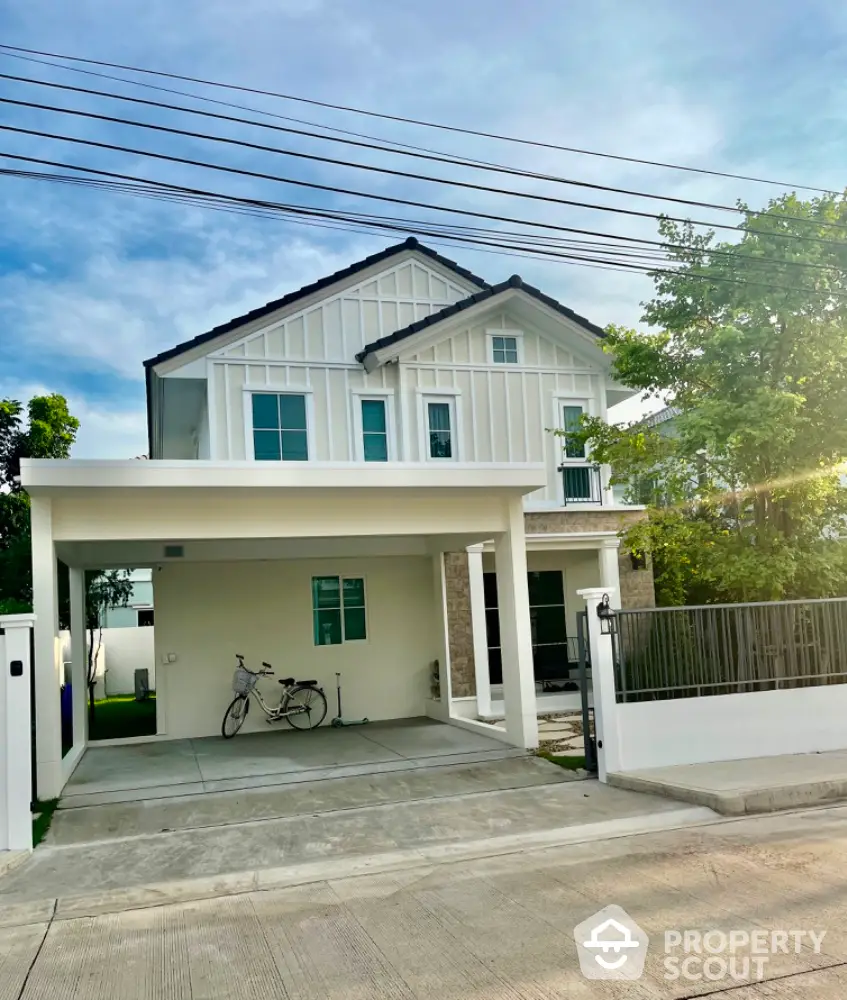 Charming two-story white house with driveway and lush greenery, perfect for family living.