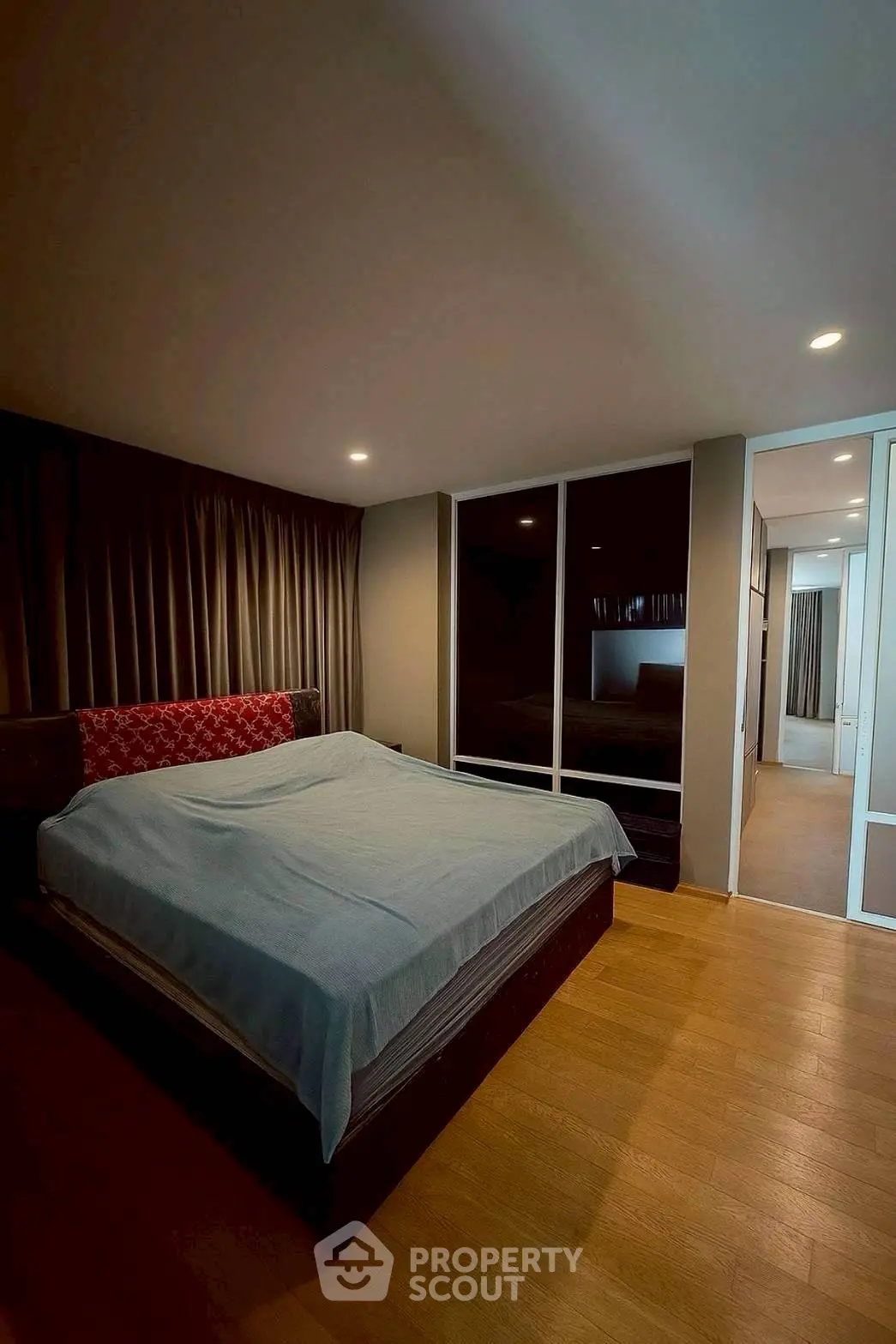 Spacious bedroom with modern design and cozy ambiance, featuring wooden flooring and large windows.