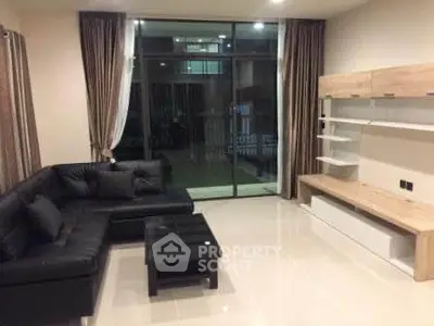 Spacious modern living room with sleek black sofa and large glass doors leading to balcony.