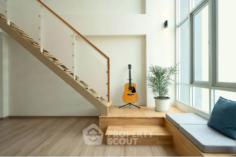 Modern minimalist living room with wooden staircase and large windows, featuring a guitar and potted plant.