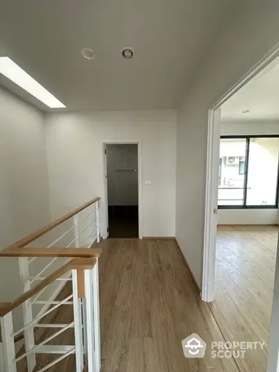 Modern interior hallway with wooden flooring and white walls leading to a bright room with large windows.