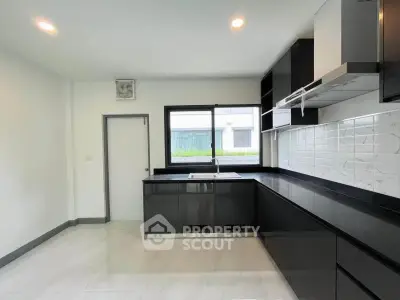Modern kitchen with sleek black cabinetry and large window for natural light.