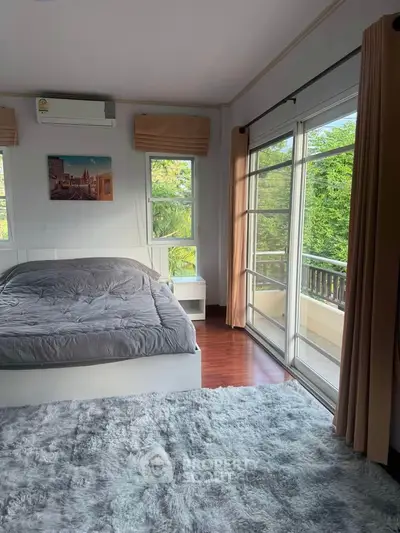 Spacious bedroom with large windows and balcony access, featuring lush greenery views.