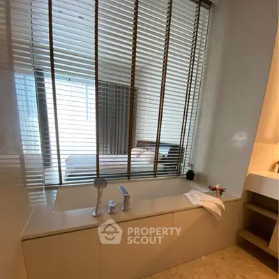 Luxurious bathroom with modern bathtub and window blinds overlooking a bedroom.