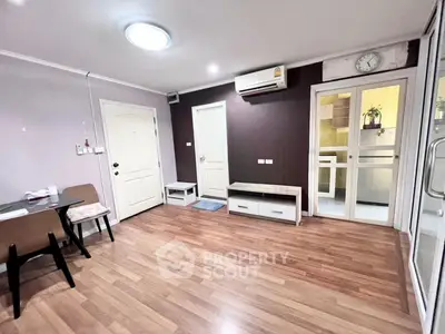 Spacious living room with modern decor and wooden flooring, featuring air conditioning and a view into the kitchen.