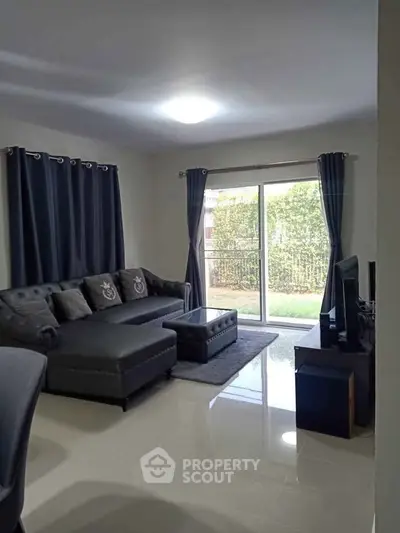 Spacious living room with modern gray sofa and large window overlooking garden.