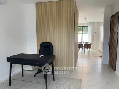 Modern home office with sleek black desk and chair, open layout leading to dining area, stylish partition wall.