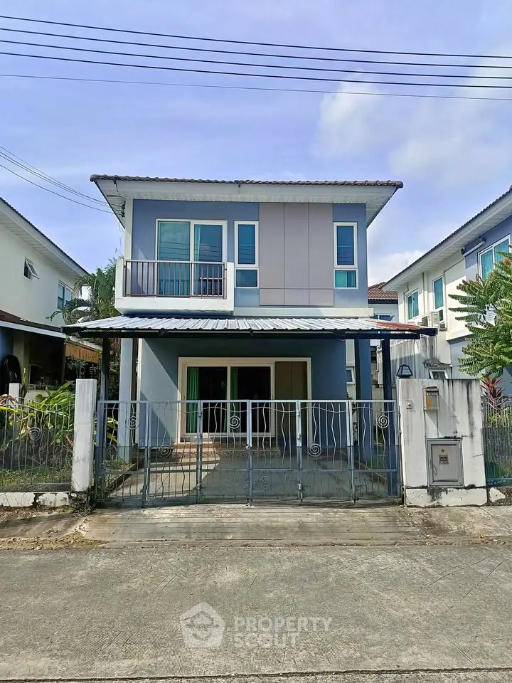 Charming two-story blue house with gated entrance and small balcony in suburban neighborhood.