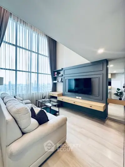 Modern living room with high ceilings and large windows, featuring a sleek TV setup.