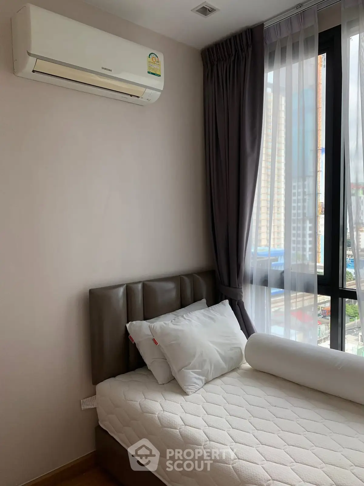 Cozy bedroom with modern air conditioning and city view through large window.