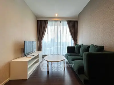 Modern living room with plush green sofa and sleek TV stand, featuring floor-to-ceiling windows and elegant curtains.
