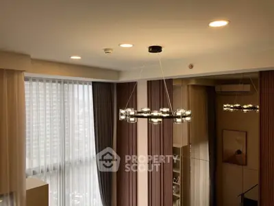 Modern living room with elegant chandelier and large windows offering city views.