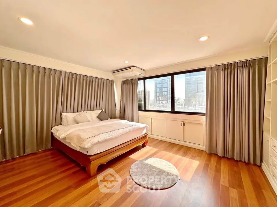 Spacious bedroom with large windows and wooden flooring in a modern apartment.