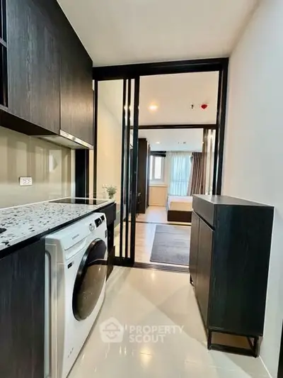 Modern apartment interior with sleek kitchen and laundry area leading to a cozy bedroom.