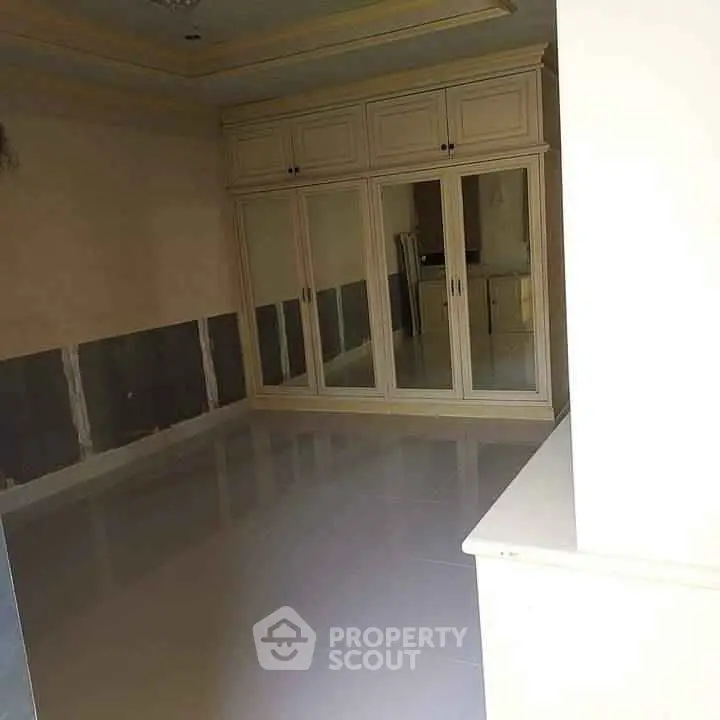 Spacious empty room with built-in mirrored wardrobe and glossy floor tiles.