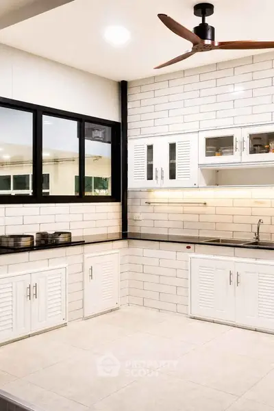 Modern kitchen with sleek white cabinetry and black countertops, featuring a ceiling fan and ample natural light.