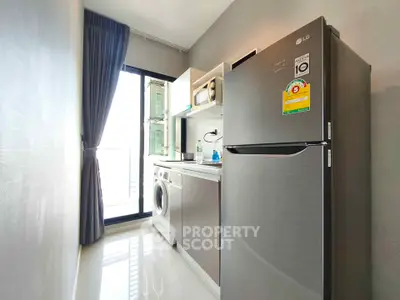 Modern kitchen with sleek appliances and natural light, featuring a washing machine and fridge.