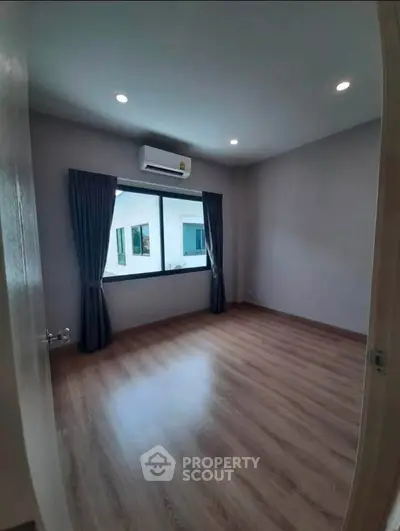 Spacious empty bedroom with wooden flooring and large window, perfect for customization.