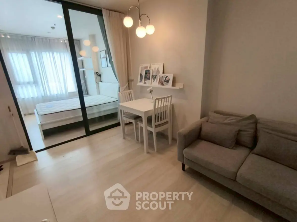 Modern living room with cozy sofa and dining area next to a bedroom with sliding glass doors.