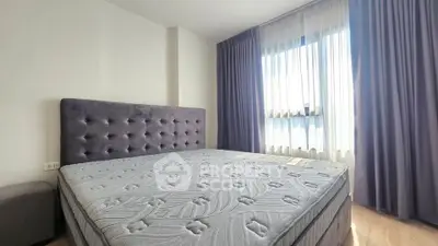 Spacious bedroom with plush headboard and large window with curtains, offering ample natural light.
