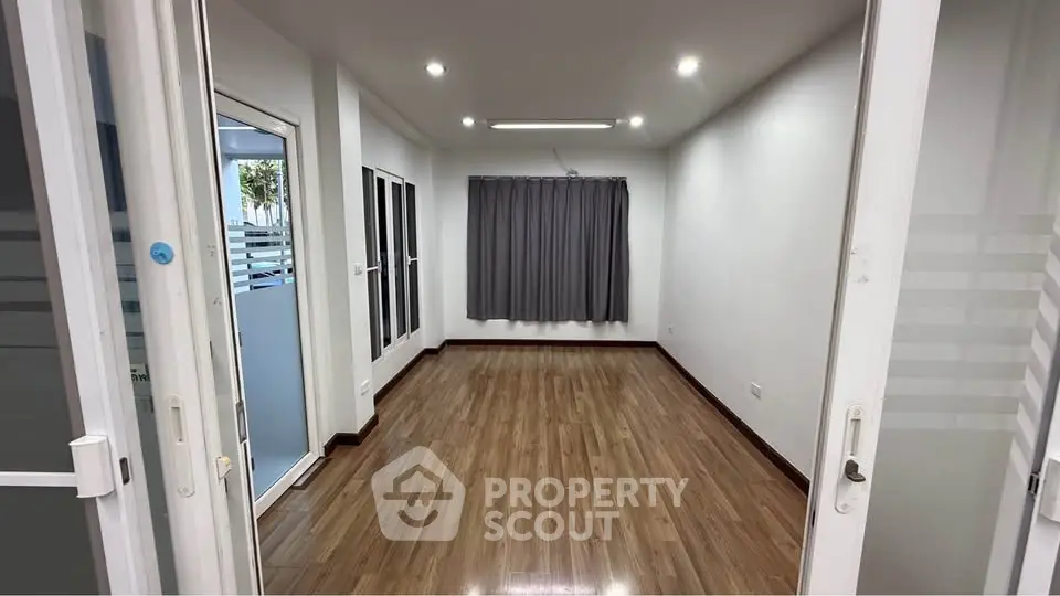 Spacious empty room with wooden flooring and large window, perfect for customization.