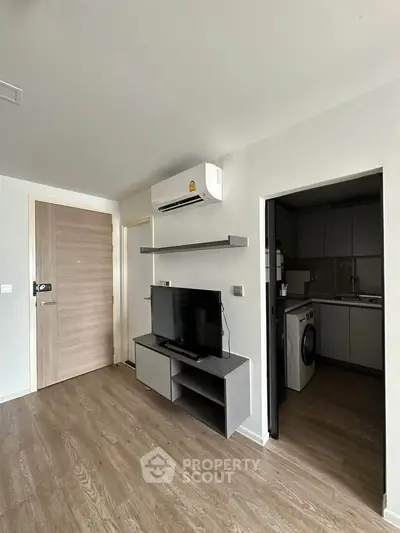 Modern apartment interior with sleek TV setup and compact kitchen area.