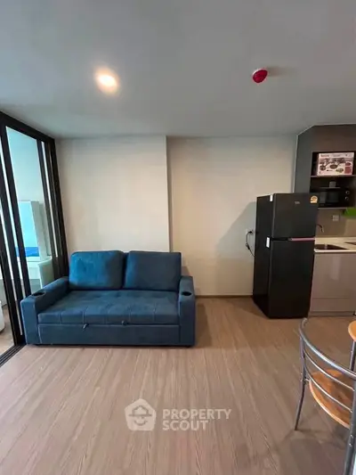Modern living room with blue sofa and sleek kitchen area featuring a fridge and dining table.