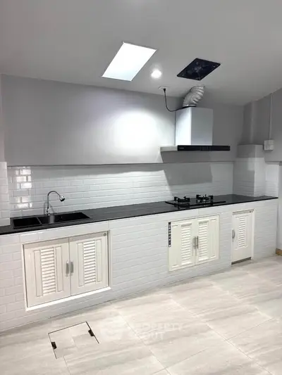 Modern kitchen with sleek black countertop and gas stove, featuring white cabinets and subway tile backsplash.