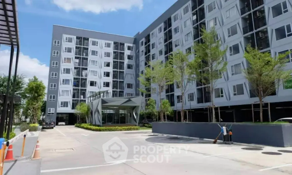 Modern apartment building exterior with landscaped entrance and clear blue sky.