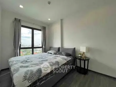 Modern bedroom with large window offering city views, featuring stylish decor and cozy ambiance.