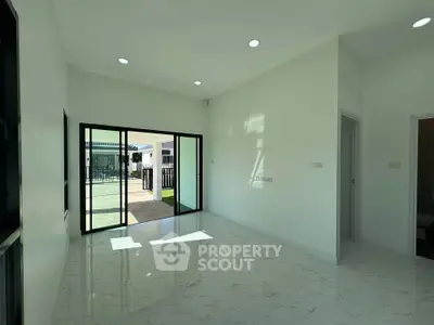 Spacious modern living room with large sliding glass doors opening to a patio, featuring sleek white tiles and recessed lighting.