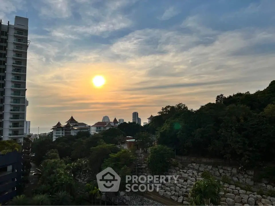 Stunning sunset view from a high-rise building overlooking lush greenery and city skyline.