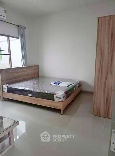 Spacious bedroom with modern wooden furniture and large window for natural light.