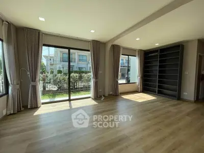 Spacious living room with large windows and built-in shelving, offering abundant natural light and garden view.