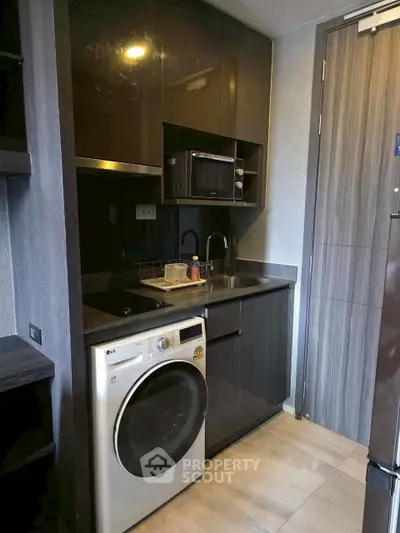Modern compact kitchen with washing machine and microwave in sleek apartment.