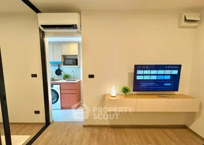 Modern living room with wall-mounted TV and view into compact kitchen with washing machine.