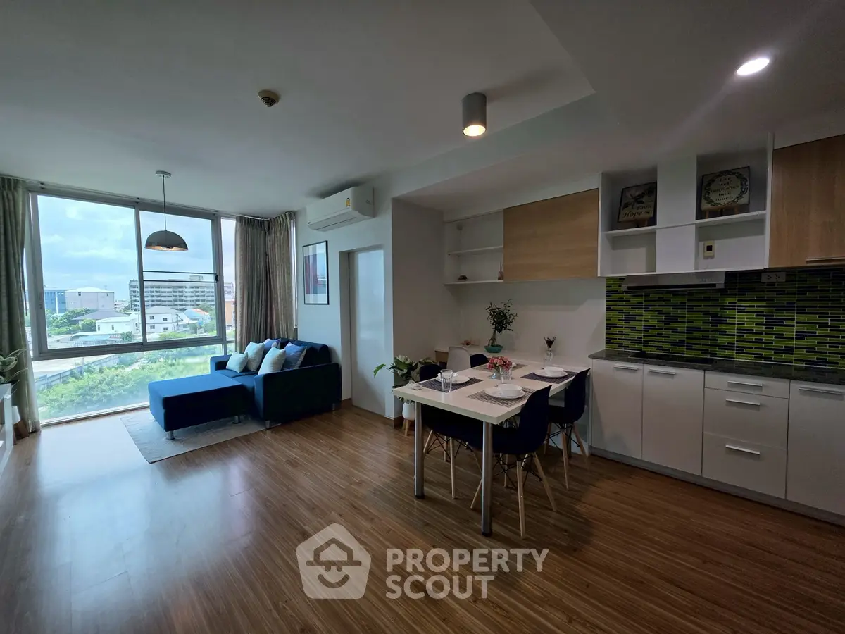 Spacious modern living room with open kitchen and large windows offering city views.