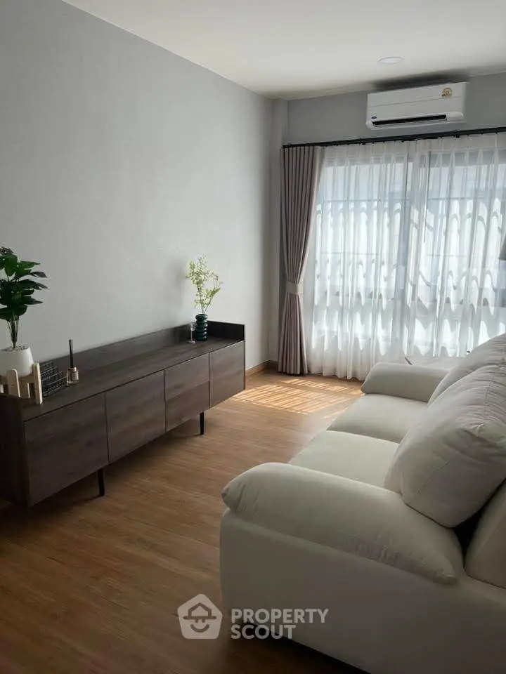 Modern living room with large window, white sofa, and wooden flooring, perfect for relaxation.
